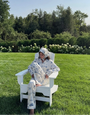 Person sitting in a white chair on a grassy lawn with trees in the background