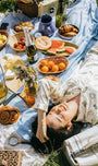 Woman lying on a picnic blanket with food and drinks