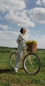 Woman in womens pajama set with button front standing by a bike in a field, enjoying the sunny sky.