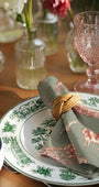 Decorative plate with a cow design, rolled napkin, and pink glass on a wooden table.