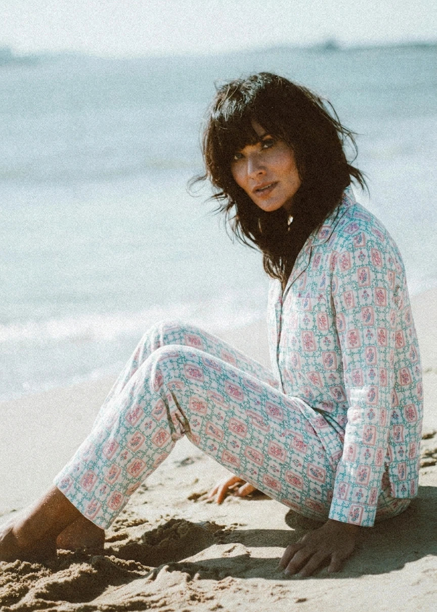 Woman sitting on the beach wearing a patterned outfit.