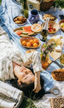 Woman lying on a picnic blanket with food and drinks wearing Oyster and Arrow organic bamboo pajamas inspired by the NorthEast Coast