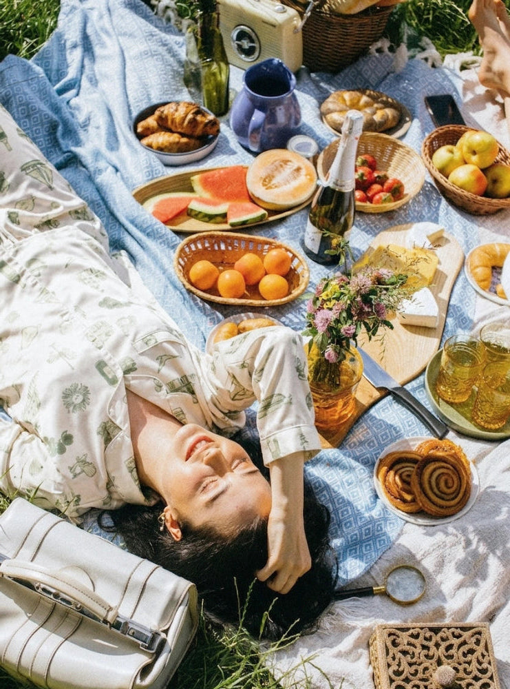 Woman lying on a picnic blanket with food and drinks wearing Oyster and Arrow organic bamboo pajamas inspired by the NorthEast Coast