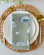 Place setting with woven placemat, white plates, gold cutlery, and a patterned napkin.