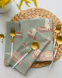 Set of green napkins with red pattern on a woven placemat with cutlery.