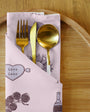Gold fork, knife, and spoon set in a decorative pink case on a wooden surface